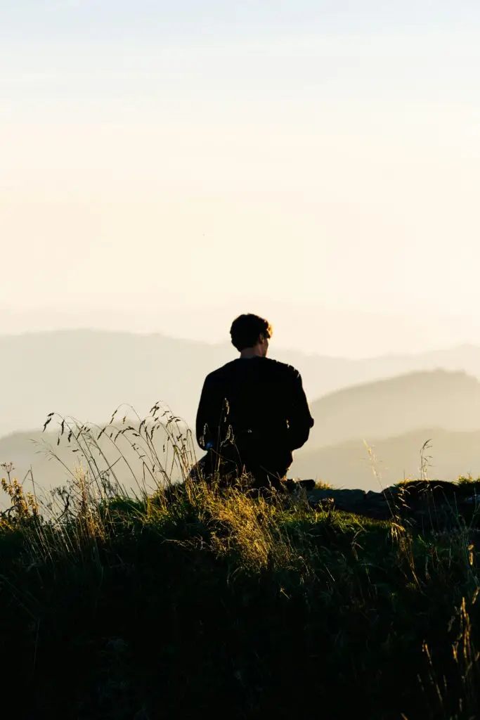 picture of a man sitting on a rock, overlooking mountains